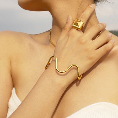A model showcasing the versatile style of the gold wave cuff bangle as part of a complete jewelry set.