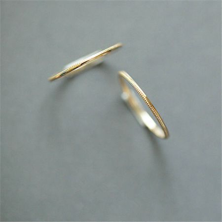 Une paire de bagues en or minimalistes de l'ensemble empilable présentées sur un fond gris neutre.