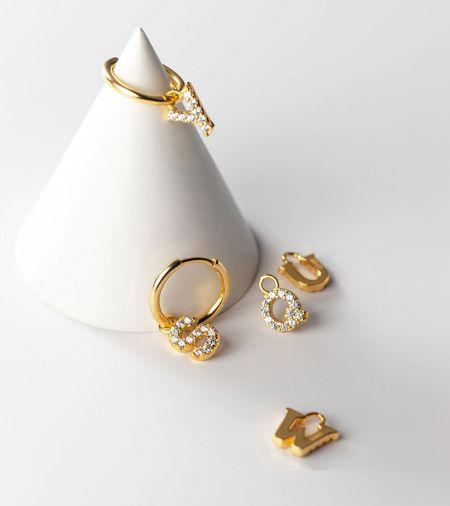 Una esposizione di vari pezzi di gioielleria iniziale in oro, tra cui orecchini a cerchio e charm con diamanti.