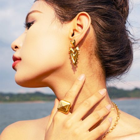 Side profile of a model wearing the 3D heart earrings as part of a complete gold jewelry set.