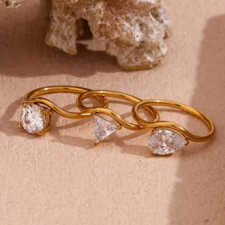 Primo piano degli anelli in acciaio inossidabile placcato oro ondulato con pietre di zirconia trasparente.