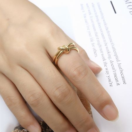 Anello a fiocco in acciaio inossidabile - Un primo piano dell'anello a fiocco in acciaio inossidabile con finitura dorata, caratterizzato da un elegante design a nodo, indossato su un dito per mostrare il suo stile e la sua vestibilità.
