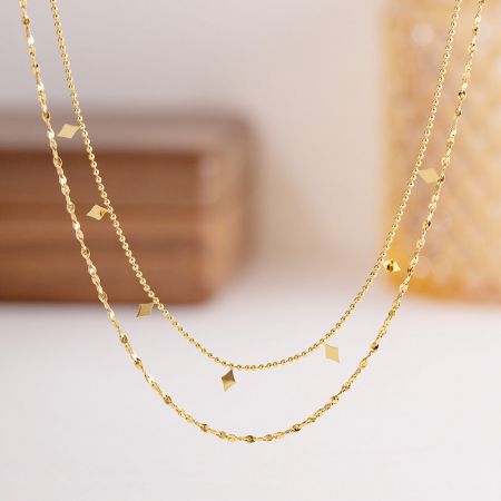 Detaillierte Produktaufnahme einer goldenen, geschichteten Halskette mit quadratischen Charms.