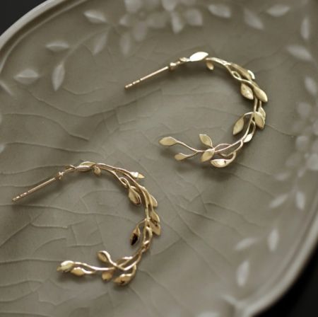 Orecchino a cerchio fogliare in argento sterling 925 - Un paio di orecchini a cerchio fogliare in argento sterling 925 con placcatura in oro, esposti su un piatto decorativo per mostrare il design intricato del ramo fogliare e i dettagli in zirconia cubica.