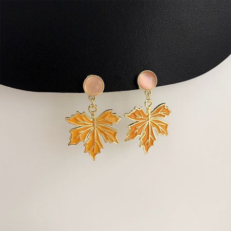 Vista completa dos brincos pendentes em forma de folha dourada e laranja com tops de pedra rosa.