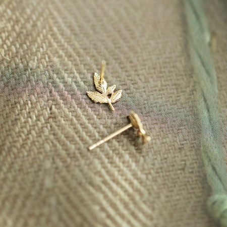 Un primo piano dettagliato degli orecchini a perno a forma di foglia d'acero dorata in argento sterling 925, evidenziando il design intricato.
