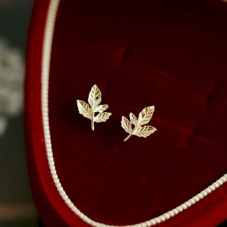 Orecchini a perno a forma di foglia d'acero dorata in argento sterling 925 (5 paia) - Un set di orecchini a perno a forma di foglia d'acero placcati in oro in argento sterling 925, esposti elegantemente in una scatola di gioielli in velluto rosso.