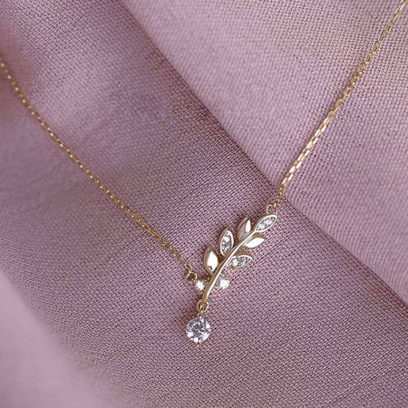 Detailed view of the gold leaf pendant necklace against a neutral background.