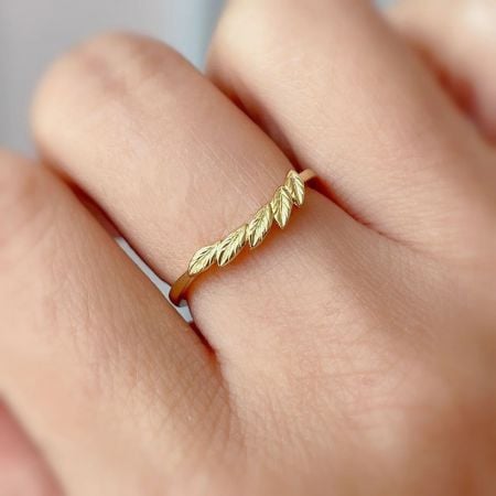 Close-up van de vergulde, bladvormige ring van sterling zilver die op een vinger wordt gedragen, met een delicate uitstraling.