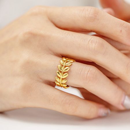 Roestvrijstalen olijftakblad gespleten open ringen (set van 5) - Een close-up van een hand die de elegante roestvrijstalen olijftakbladring met een mooie gouden afwerking draagt, waarbij het verstelbare open ontwerp wordt getoond.