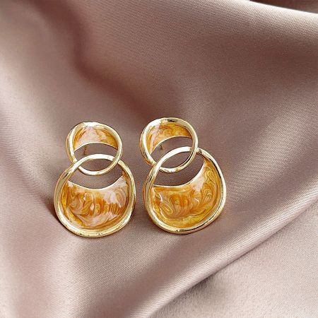 Vue détaillée des boucles d'oreilles à clou à double boucle, montrant la finition dorée brillante et l'émail marbré dans des teintes de chameau, blanc et jaune.
