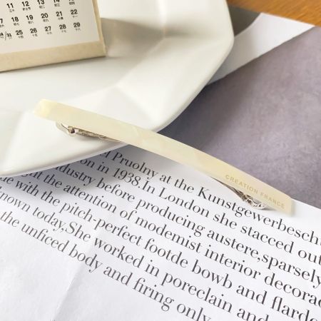 A single long acetate hair clip displayed on a white plate, highlighting its sleek design.