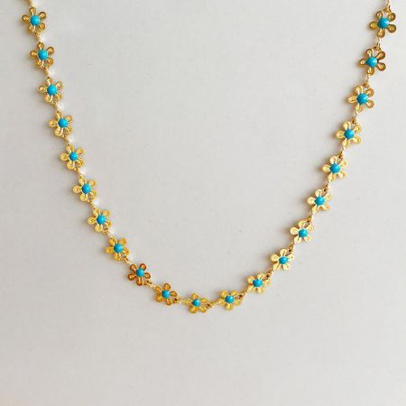 Uno scatto dettagliato del prodotto della collana dorata con perline a forma di fiore turchesi.