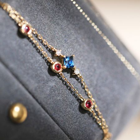 Detaillierte Ansicht der geschichteten Goldkette und der lebhaften Anordnung von Edelsteinen am Silberarmband.
