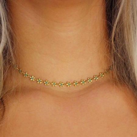 Scatto dettagliato della collana con charm a forma di fiore di camomilla su uno sfondo semplice, evidenziando lo smalto blu.