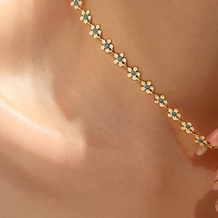 Un'altra angolazione della collana dorata che mostra i link a forma di fiore e i dettagli in smalto blu.