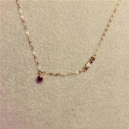 Vista detallada del collar de oro con el colgante de gema roja oscura y cuentas de oro.