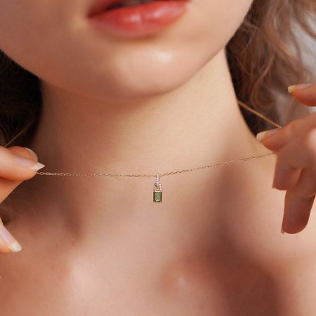 Collar con colgante de cerradura pequeña de zirconia verde en plata esterlina 925 - Un modelo que lleva el elegante collar de plata esterlina 925 con un pequeño colgante de cerradura de zirconia verde, mostrando su diseño delicado y acabado en oro.