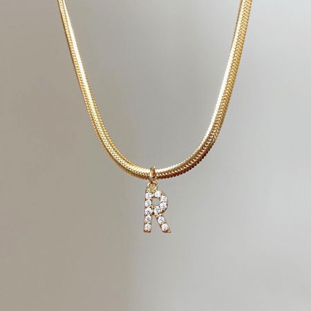 Gedetailleerd uitzicht op de elegante 'K' initialenhanger aan een gouden slangenketting.