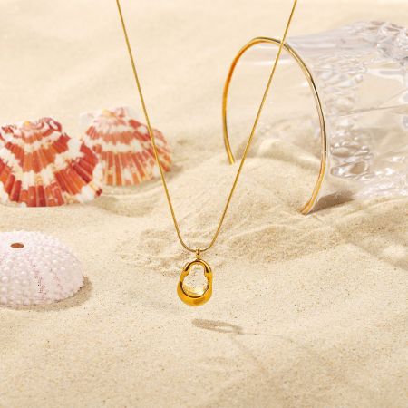 Imagen de estilo de vida del collar de colgante ovalado en tono dorado en un entorno de playa.