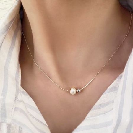 Una versión en tono dorado del collar de perlas y cuentas, exhibida sobre una superficie blanca.