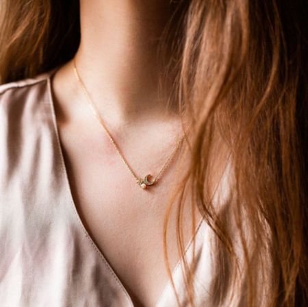 Goldplattierte Halskette mit Mond und Stern, die getragen wird, um ihre elegante Länge und ihren Stil zu präsentieren.