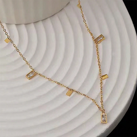 Dettaglio ravvicinato di una collana dorata del set con charm in pietra chiara rettangolare.