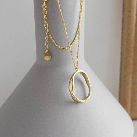 Le collier pendentif ovale irrégulier dans une finition plaquée or 18K époustouflante, exposé sur un support.