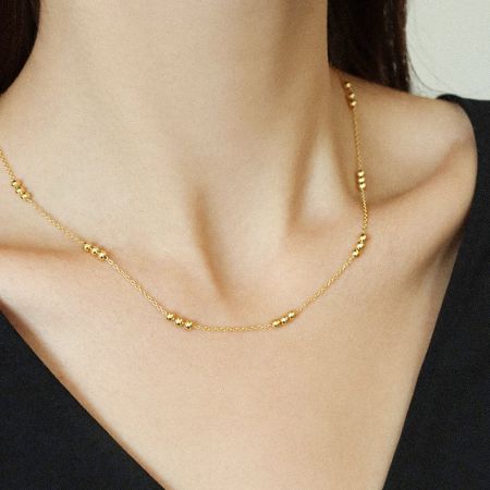 Frau in einem schwarzen Oberteil, die die zarte goldene Perlenkette trägt.