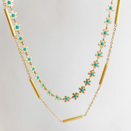 La collana in acciaio inossidabile arrotolata per mostrare il suo intricato motivo floreale con accenti turchesi.