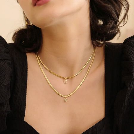 Model dat een gelaagde look toont met de 'C' en 'K' initialenkettingen.