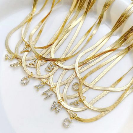 Roestvrijstalen pave A-Z initialen letter slangenketting set - Een collectie van roestvrijstalen goudkleurige slangenkettingen, elk met een sprankelende pave A-Z initialenletterhanger.