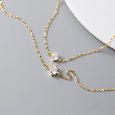Una coppia di bracciali in argento sterling placcato oro con un singolo zirconio scintillante, che mette in mostra il design elegante.