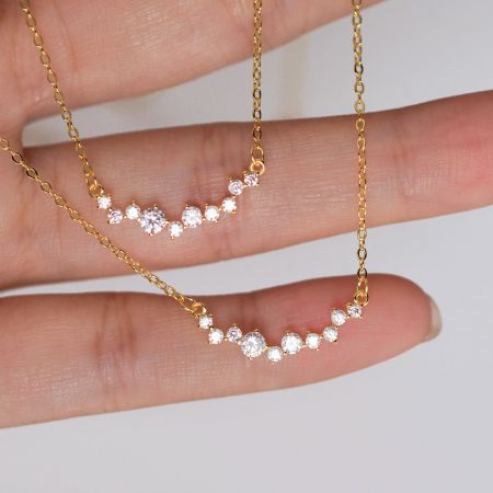 Close-up of two gold-plated 925 silver smile necklaces with CZ stones, held in hand to show detail.