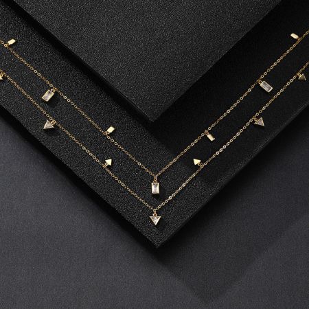 Due collane con charm geometrici presentate in una scatola nera per gioielli, evidenziando il loro design elegante.