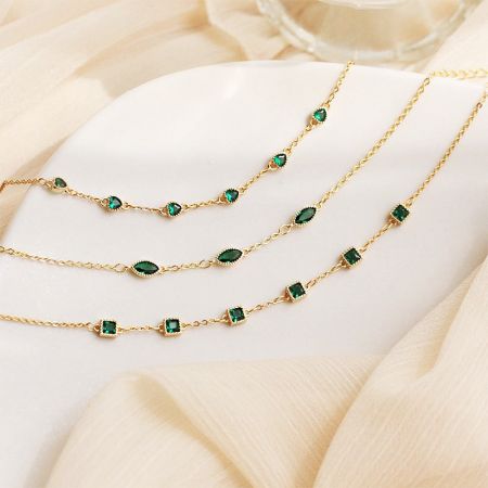 Close-up of three gold-plated sterling silver bracelets, each featuring a different green gemstone shape: square, eye, and heart.