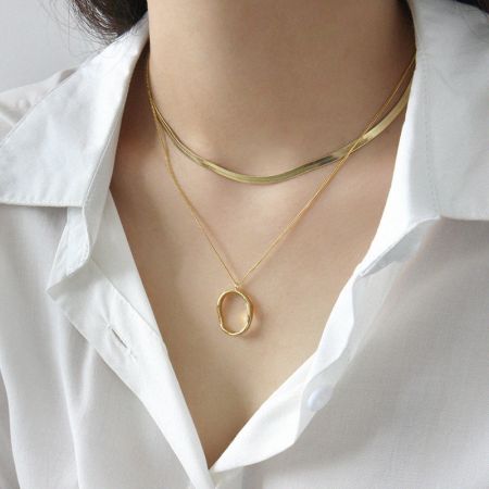 Un modèle présentant le look superposé du collier pendentif ovale irrégulier en or pour un style chic au quotidien.