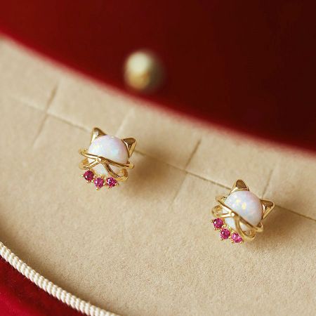 Primo piano di un orecchino a forma di gatto in oro con opale e gemme rosa.