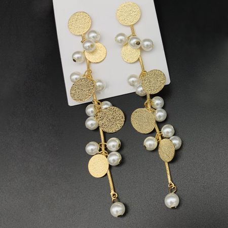 Vue rapprochée des boucles d'oreilles pendantes plaquées or, mettant en valeur les disques texturés et les perles blanches lisses.
