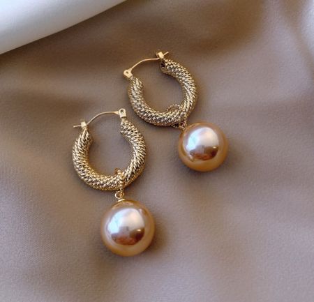 Gros plan détaillé de la boucle d'oreille huggie vintage en or plaqué et du capuchon en perle.