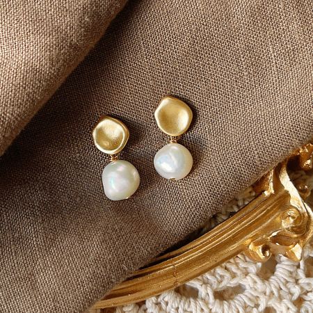 Um par de brincos de pérola barroca em ouro 14k com acabamento fosco, destacando seu design elegante.
