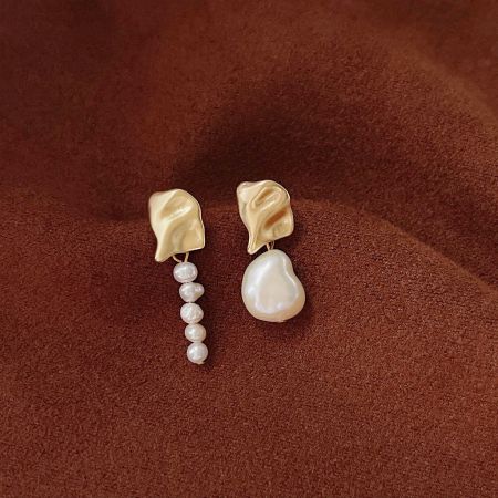A pair of gold earrings with a leaf-like design and dangling baroque pearl elements.
