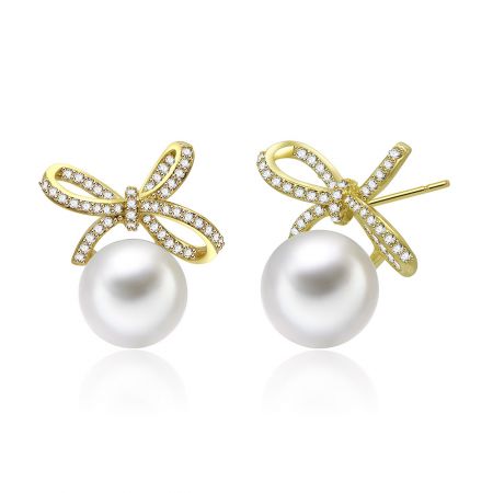 Vue rapprochée des boucles d'oreilles pendantes en or perlé, mettant en valeur la grande perle blanche et le nœud en or.