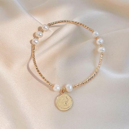 Close-up of the Queen Elizabeth II coin pendant on the gold and pearl bracelet.