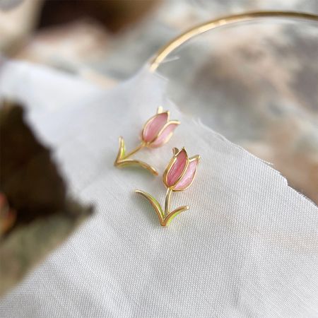 Vue rapprochée des boucles d'oreilles en tulipe en or et émail rose sur un fond neutre.