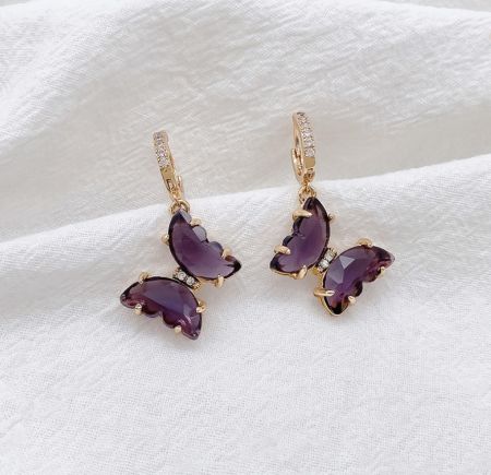 Vue latérale des boucles d'oreilles huggie en or et violet, mettant en valeur le design délicat de papillon et le sertissage de pierres précieuses.