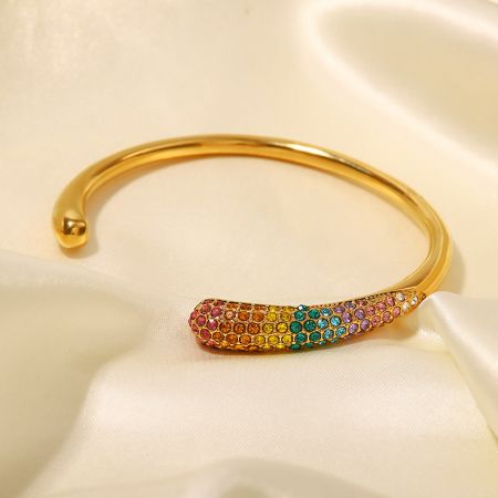 鮮やかな虹色のキュービックジルコニアストーンが並ぶゴールドカフバングルのクローズアップ。