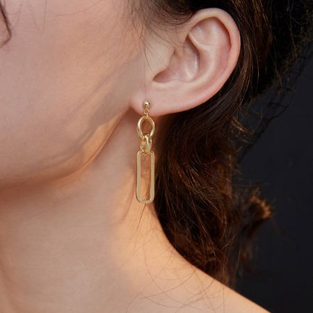 Modelo usando los pendientes colgantes rectangulares de oro para mostrar escala y estilo.