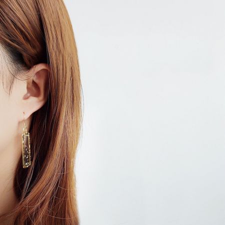 幾何学的な長方形の樹脂ドロップイヤリングを着用したモデルが、そのスケールと優雅なドレープを披露しています。