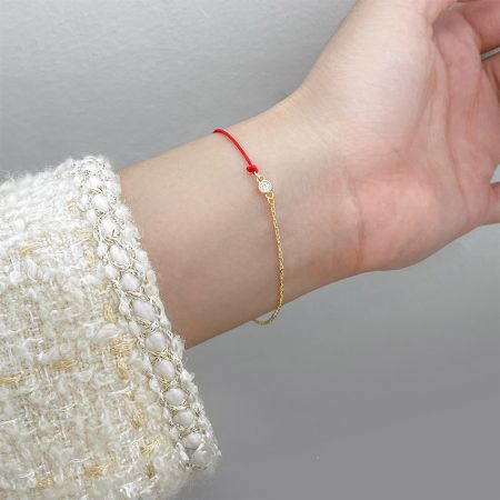 Modelo usando la pulsera minimalista de hilo rojo y cadena de oro, mostrando su delicado diseño en la muñeca.